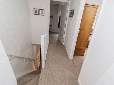 A carpeted hallway with stairs and an open door showing a wooden wardrobe at Lavender Cottage in South Zeal