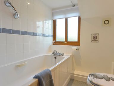 A bathroom with a bathtub a towel on the edge a window with frosted glass and a toilet with a decorative seat at Lavender Cottage in South Zeal