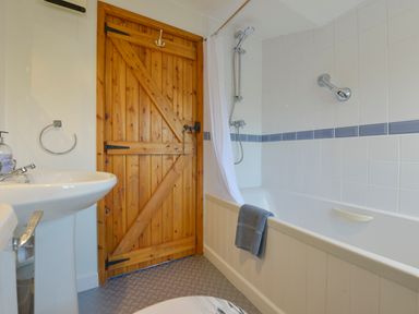 A bathroom with a white sink wooden door and a bathtub with white tiles and blue towel at Lavender Cottage in South Zeal
