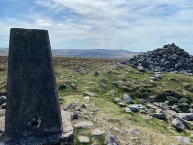 An outdoor scene with a stone trig point and a large pile of rocks on grassy terrain at Lavender Cottage in South Zeal
