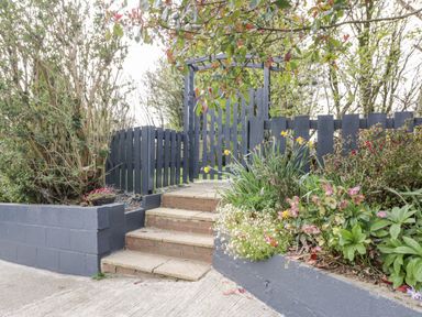 An outdoor garden area with flower beds stone steps and a wooden gate and fence at Westfields in Kennards House near Launceston