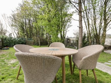 An outdoor wooden round table with four wicker chairs on grass surrounded by trees at Westfields Kennards House near Launceston