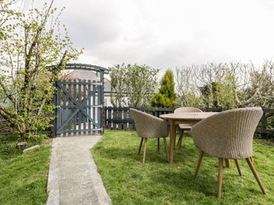 A garden with a table and three chairs on grass next to a wooden gate at Westfields in Kennards House near Launceston