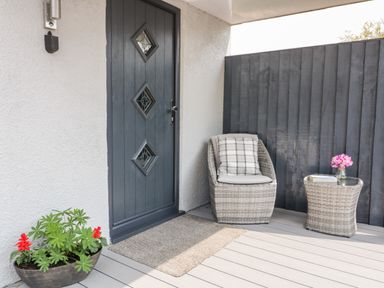 A porch with a gray door a wicker chair with cushion and small table with flowers at Westfields Kennards House near Launceston