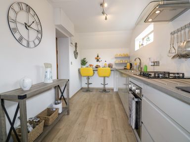 A kitchen with wooden floor a wall clock and yellow bar stools at Westfields in Kennards House near Launceston