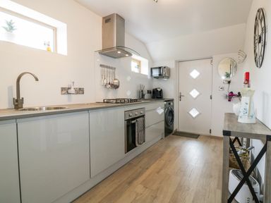 A kitchen with cabinets a sink stovetop oven washing machine microwave and a wooden table with a clock on the wall at Westfields in Kennards House near Launceston