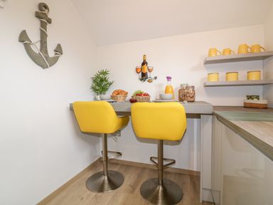 A kitchen corner with two yellow bar stools a wooden table with food and drink a decorative anchor on the wall at Westfields in Kennards House near Launceston