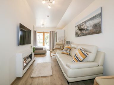 A living room with a white sofa with striped cushions a white fireplace and a wall mounted TV at Westfields Kennards House near Launceston