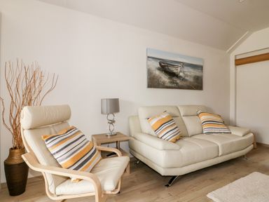 A living room with a beige sofa and chair with striped cushions a wooden side table with a lamp and a painting of a boat on the wall at Westfields in Kennards House near Launceston