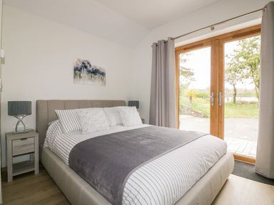 A bedroom with a bed nightstands lamps and glass doors opening to an outdoor area at Westfields Kennards House near Launceston