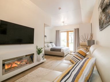 A living room with a fireplace a wall-mounted TV a beige sofa and a bed near glass doors at Westfields Kennards House near Launceston