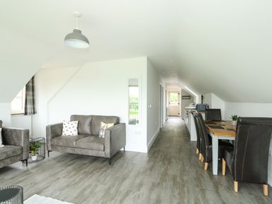 An open plan living and dining area with grey sofas, a dining table with black chairs and a kitchen along a corridor at The Attic in Blackborough End near Kings Lynn