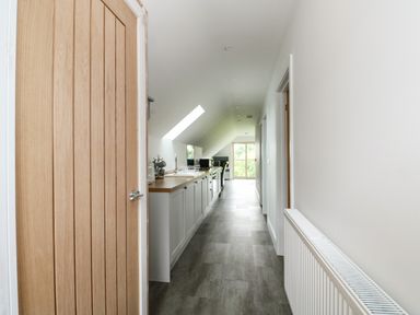 A hallway with a wooden door and radiator leading to a kitchen area with cabinets and a skylight at The Attic in Blackborough End near Kings Lynn