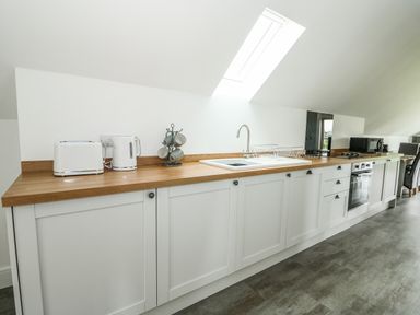 A kitchen with white cabinets a wooden countertop a toaster kettle mugs stove oven microwave and dining area at The Attic in Blackborough End near Kings Lynn