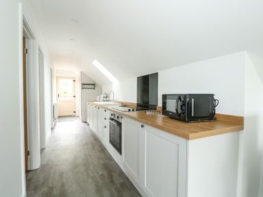 A long kitchen with white cabinets wooden countertop microwave oven stove and sink at The Attic in Blackborough End near King's Lynn