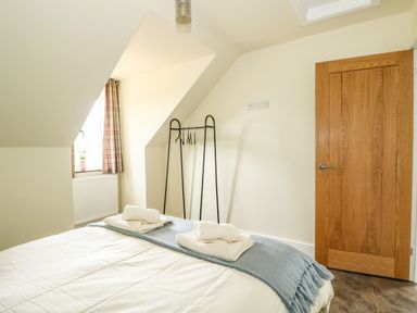 A bedroom with a bed with towels on a blanket a wooden door a window with curtains and a clothes rack at The Attic in Blackborough End near Kings Lynn