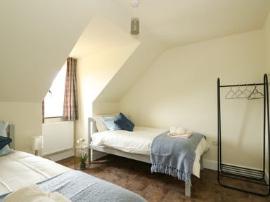 A bedroom with two single beds a window with plaid curtains a small round table and a clothes rack at The Attic in Blackborough End near Kings Lynn