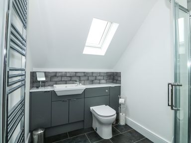 A bathroom with a toilet sink gray cabinets tiled backsplash skylight and glass shower door at The Attic in Blackborough End near Kings Lynn