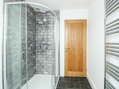 A bathroom with a glass enclosed shower with gray tiles a wooden door and a chrome heated towel rail at The Attic in Blackborough End near Kings Lynn