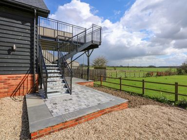 Metal staircase leading to an elevated patio beside a building with a gravel and paved patio area and a view of fenced green fields at The Attic in Blackborough End near King's Lynn