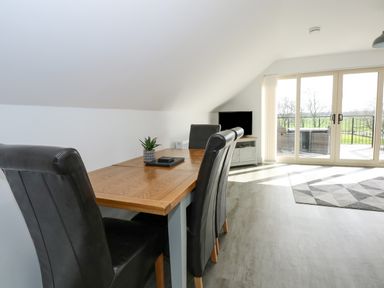 A dining table with black chairs and a small plant beside sliding glass doors with a view of a balcony and greenery at The Attic in Blackborough End near King's Lynn