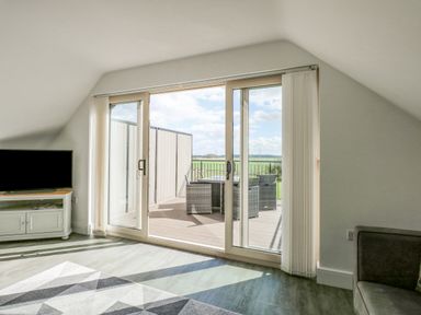 A living room with a television, a rug, sliding glass doors, and outdoor furniture at The Attic in Blackborough End near Kings Lynn