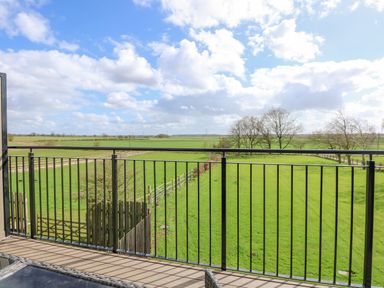 A view of green fields and trees from a balcony with a black metal railing at The Attic in Blackborough End near King's Lynn
