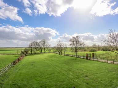 A large green lawn with a wooden fence and trees under a blue sky at The Attic Blackborough End near King's Lynn