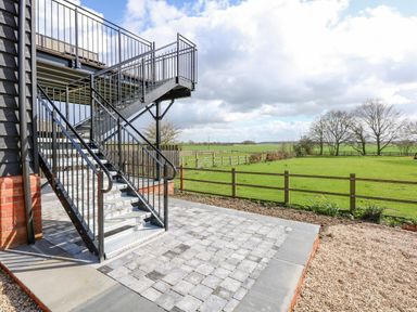 A metal staircase and paved patio leading to a fenced green field at The Attic in Blackborough End near Kings Lynn