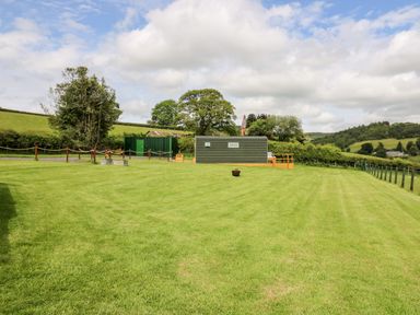 A green lawn with a small building and trees in the background at Hwyl Rhayader near Llandrindod Wells