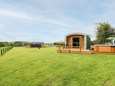 Two wooden pods on a grassy field with outdoor seating and a hot tub at Hwyl Rhayader near Llandrindod Wells