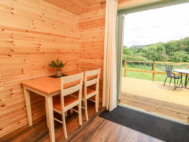 A small dining area with a wooden table and two chairs next to an open door leading to a deck with outdoor furniture at Hwyl in Rhayader near Llandrindod Wells