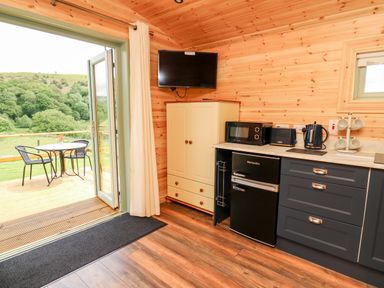 A kitchen area with cabinets, a microwave, toaster, kettle, mini fridge, and a door leading to an outdoor patio with a table and chairs at Hwyl Rhayader near Llandrindod Wells