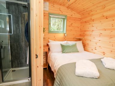A bedroom with a bed next to a small window and an adjacent shower enclosure at Hwyl Rhayader near Llandrindod Wells