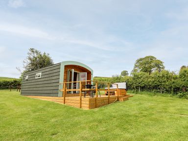 A small cabin with wooden deck and outdoor table and chairs on a grassy lawn at Hwyl Rhayader near Llandrindod Wells