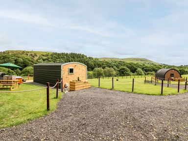 Two small wooden cabins with curved roofs on grassy land with fenced areas and picnic table at Hwyl Rhayader near Llandrindod Wells