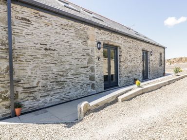 Exterior of a stone building with two black framed glass doors and small plants in pots at The Cornstore in Helland near Bodmin