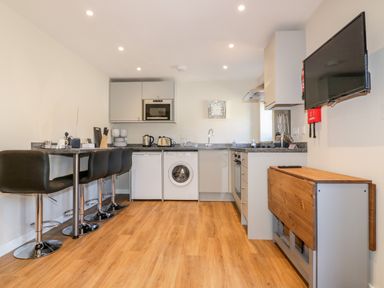 A kitchen with bar stools a washing machine and a wall mounted television at The Cornstore in Helland near Bodmin