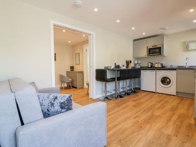 A living room with a grey sofa and black bar stools at a kitchen counter and wood flooring at The Cornstore in Helland near Bodmin