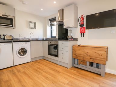 A kitchen with washing machine oven microwave wooden folding table and wall mounted television at The Cornstore in Helland near Bodmin