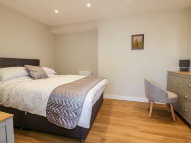 A bedroom with a bed a chair a dresser a lamp and a framed picture on the wall at The Cornstore in Helland near Bodmin