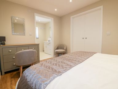 A bedroom with a bed, a dresser with a mirror above it, a chair, and an open door leading to a bathroom at The Cornstore in Helland near Bodmin