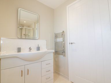 A bathroom with a white sink vanity unit and mirror above and a towel radiator on the wall at The Cornstore Helland near Bodmin