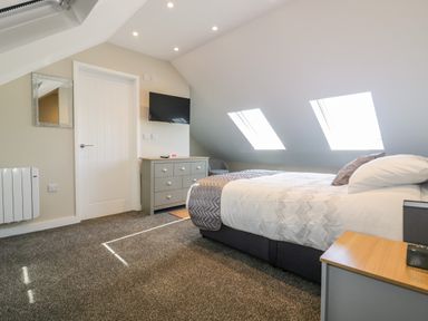 A bedroom with a bed a dresser a wall-mounted television and skylight windows at The Cornstore in Helland near Bodmin