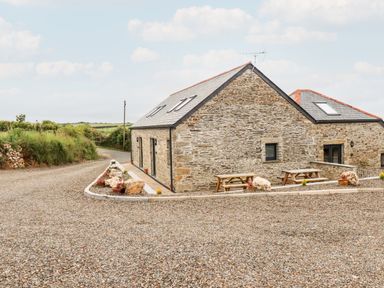 A stone house with a slate roof and picnic tables on a gravel area at The Cornstore in Helland near Bodmin
