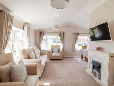 A living room with beige sofas curtains and a wall-mounted TV at 12 Bucklesham Park in Bucklesham near Trimley St Martin