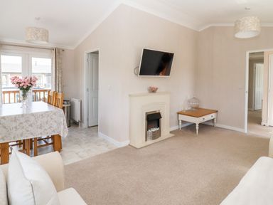 A living room with a fireplace a wall mounted tv a dining table with flowers and chairs at 12 Bucklesham Park in Bucklesham near Trimley St Martin