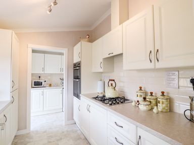 A kitchen with white cabinets a stove kettle countertop canisters and a microwave in the adjoining room at 12 Bucklesham Park Bucklesham near Trimley St Martin
