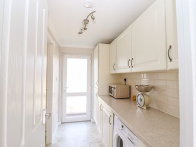 A utility room with white cabinets a washing machine a microwave and a weighing scale at 12 Bucklesham Park in Bucklesham near Trimley St Martin