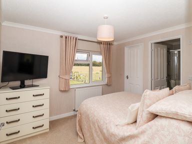 A bedroom with a bed pillows a chest of drawers with a television and a window with curtains at 12 Bucklesham Park in Bucklesham near Trimley St Martin